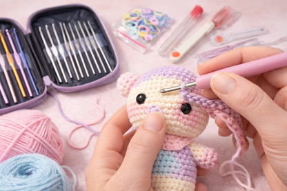 Person crocheting a small plush toy with yarn and crochet hooks kit tools on a pink surface